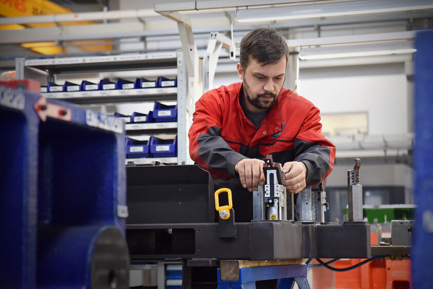 Na obrázku je technik výroby nástrojů ze společnosti weba, který se soustředí na montáž měřidla zkušebního dílu ve výrobním prostředí. Scéna je obklopena nástroji, stroji a dalšími pracovními pomůckami. Technik pracuje přesně a pečlivě, aby zajistil správné sestavení měřidla. Atmosféra vyzařuje profesionalitu a efektivitu, když technik připravuje měřidlo k použití ve výrobě. Obrázek ilustruje zastřešující odbornost společnosti weba v oblasti technologie tváření.