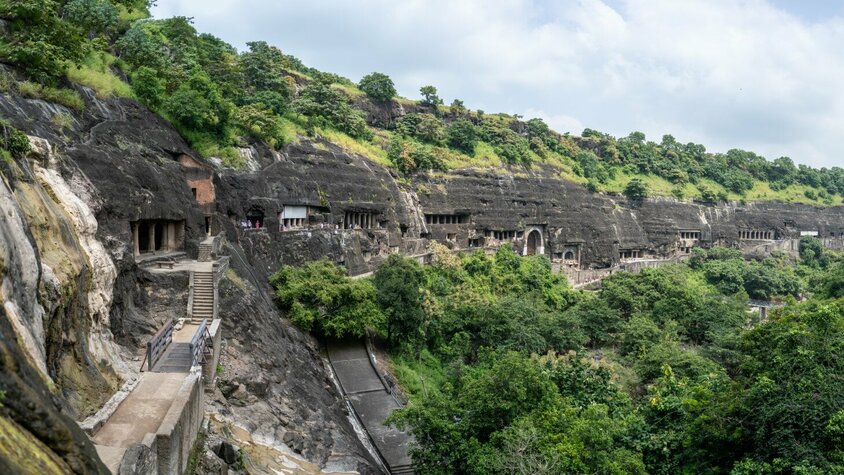 Antike Höhlenarchitektur inmitten üppiger Natur Eine beeindruckende Reihe von Höhlen, in Fels gemeißelt, eingebettet in eine grüne Hügellandschaft, mit Zugangswegen, die durch die steilen Klippen führen.