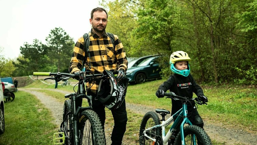 Familienzeit auf zwei Rädern – Radek mit seinem Sohn Radek Šimek steht mit Mountainbike und Helm neben seinem jungen Sohn, der mit Kinder-MTB und Helm startklar ist.