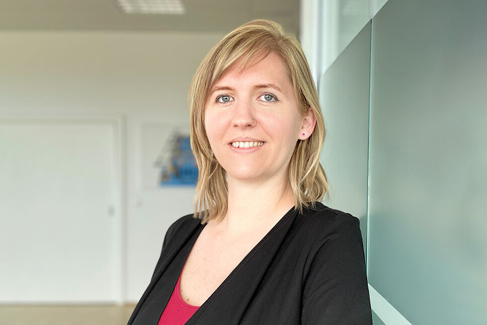 Porträt von Tanja Burghuber, Personalmanagerin bei weba Werkzeugbau, entspannt an einer Milchglaswand in Dietach lehnend, mit einem professionellen und freundlichen Ausdruck, betont durch die weiche Beleuchtung und den verschwommenen Hintergrund.