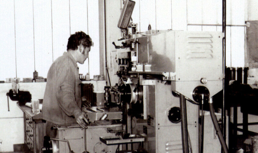 Černobílý snímek z 80. let 20. století zachycuje obráběcího technika, který obsluhuje konvenční vyvrtávačku.