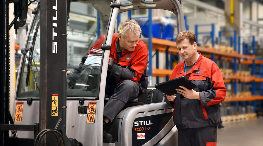 Two toolmaking technicians discuss the logistics of series production for press hardening. One is sitting in the forklift and looking at the tablet that the other toolmaking technician is holding in his hand.