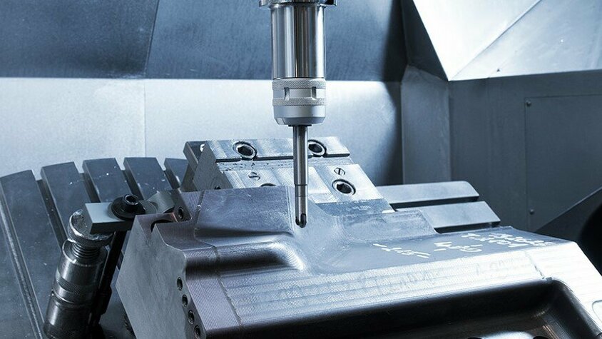 CNC-Fräsen eines Stahleinsatzes in der Lohnfertigung Innenaufnahme eines CNC-Bearbeitungszentrums bei der Lohnfertigung, während es einen Stahleinsatz fräst.