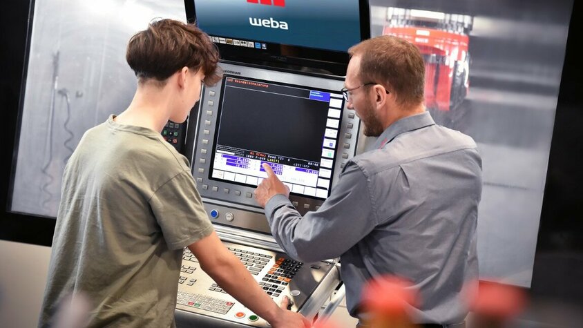 Lehre in Steyr - Ausbildung als Zerspanungstechniker Ein Ausbilder erklärt einem Lehrling in der Zerspanungstechnik die Bedienfunktionen an der Steuerung eines Bearbeitungszentrums. In der Lehre in Steyr bei weba Werkzeugbau liegt der Fokus auf praxisnaher Ausbildung direkt an Maschinen.