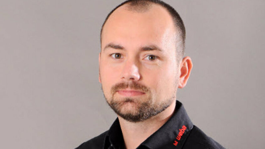 Radek Šimek – Projektmanager bei weba Porträt von Radek Šimek, Projektmanager bei weba Werkzeugbau, im schwarzen Firmenhemd vor neutralem Hintergrund.