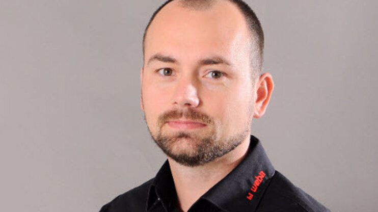 Porträt von Radek Šimek, Projektmanager bei weba Werkzeugbau, im schwarzen Firmenhemd vor neutralem Hintergrund.